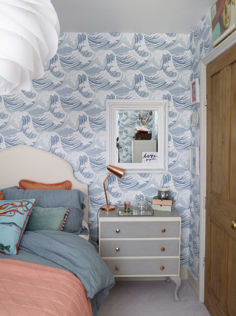 Bedroom styled by Maxine Brady featured wave-patterned wallpaper and an upholstered bed with coral and blue cushions.