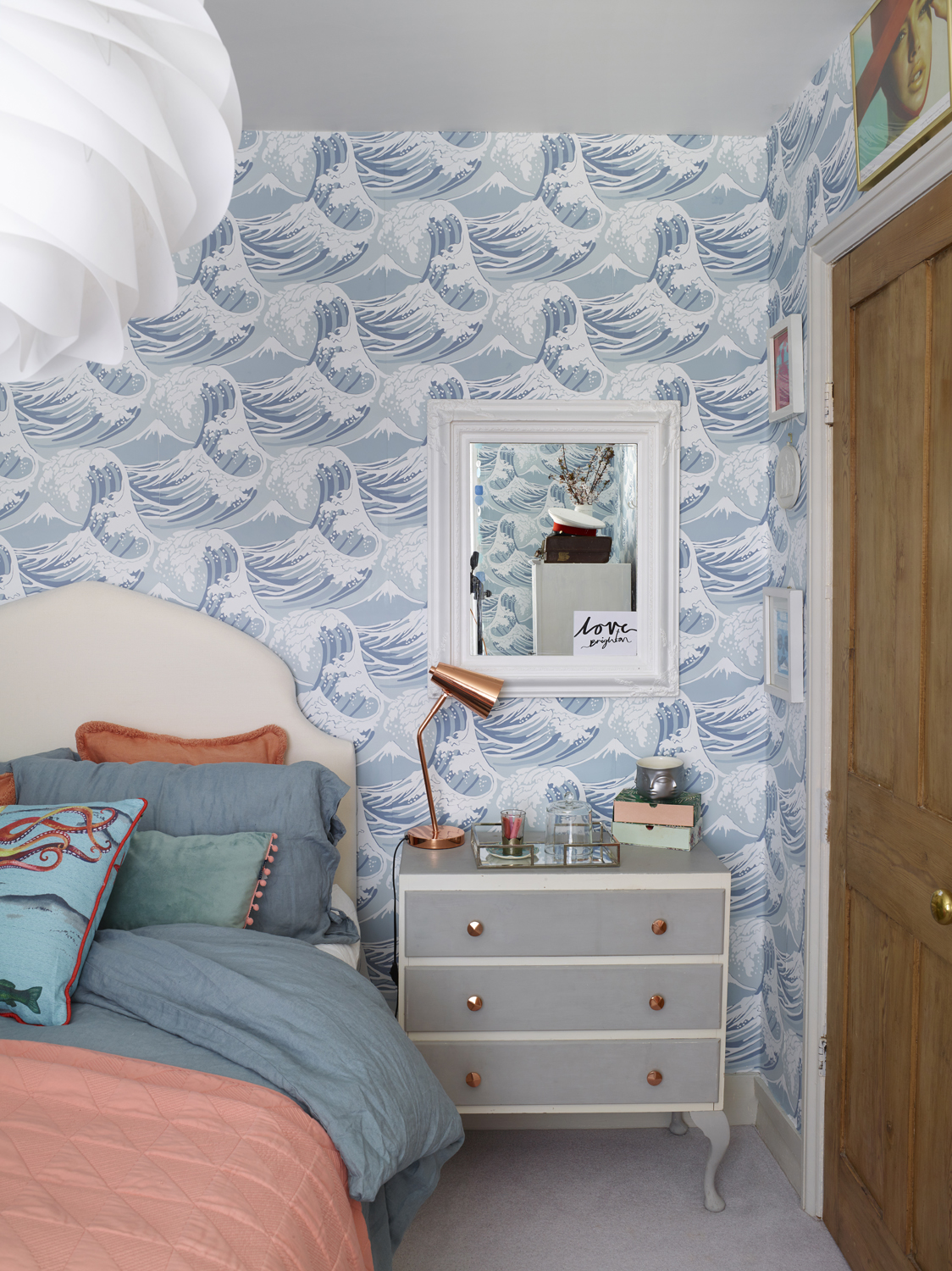 Bedroom styled by Maxine Brady featured wave-patterned wallpaper and an upholstered bed with coral and blue cushions.