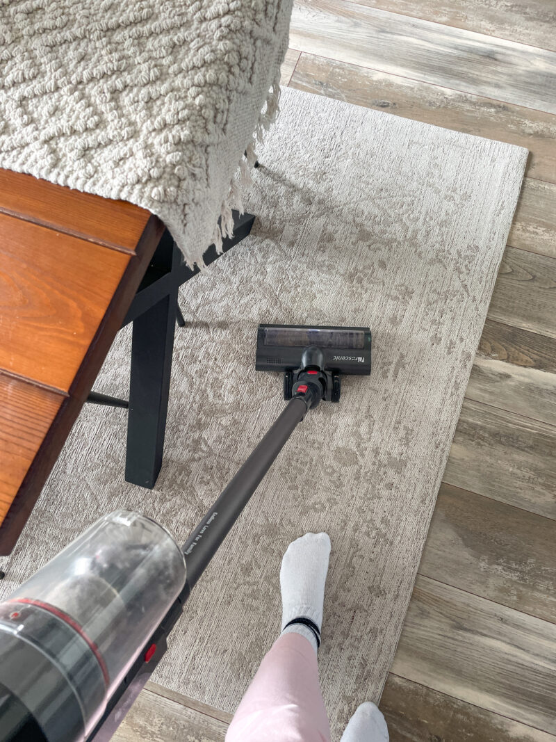 Woman's feet on a rug with a vacuum cleaner.