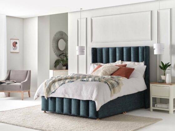 Amersham winged upholstered bed in blue velvet with rust coloured cushion and off white walls.