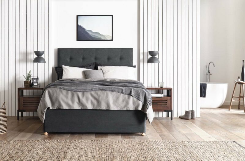 Dark grey upholstered bed in a white bedroom with dark-brown acacia bedside tables.