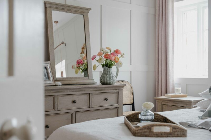 Oak Furnitureland weather oak Burleigh chest of drawers with matching mirror in a white and pink bedroom.
