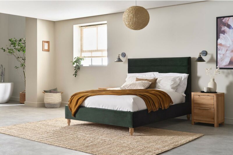 Bottle green velvet upholstered bed in neutral bedroom with earthy tones and oak furniture.