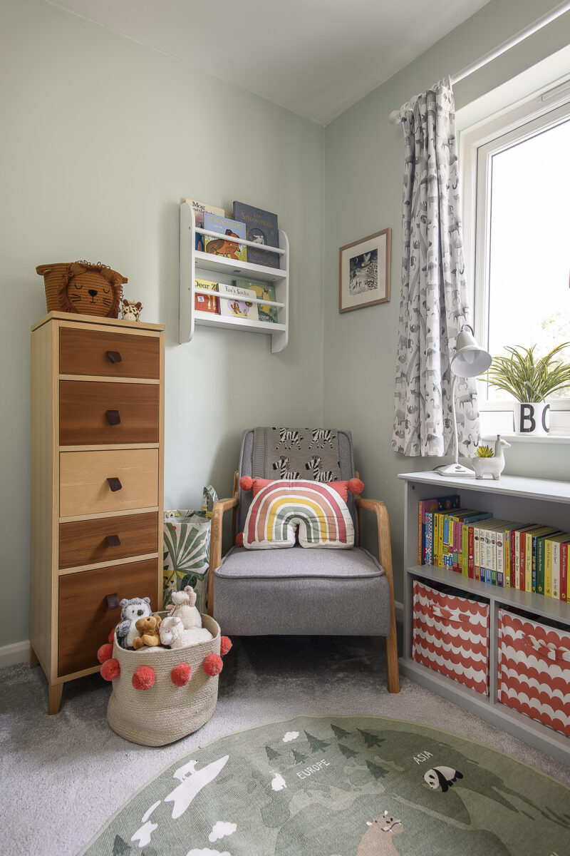 Children's bedroom with a grey chair in the corner, books, a tallboy unit and colourful accessories.