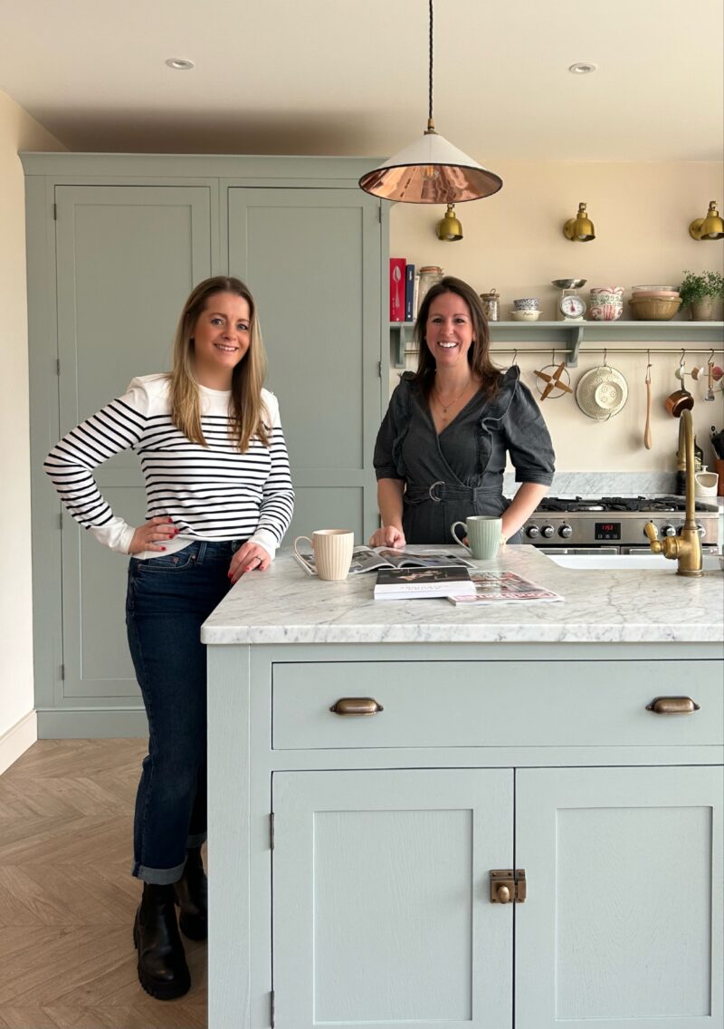 Founders of Nest Magazine, Charlotte Luxford and Sophie Vening stand together in a pale blue and marble topped kitchen.