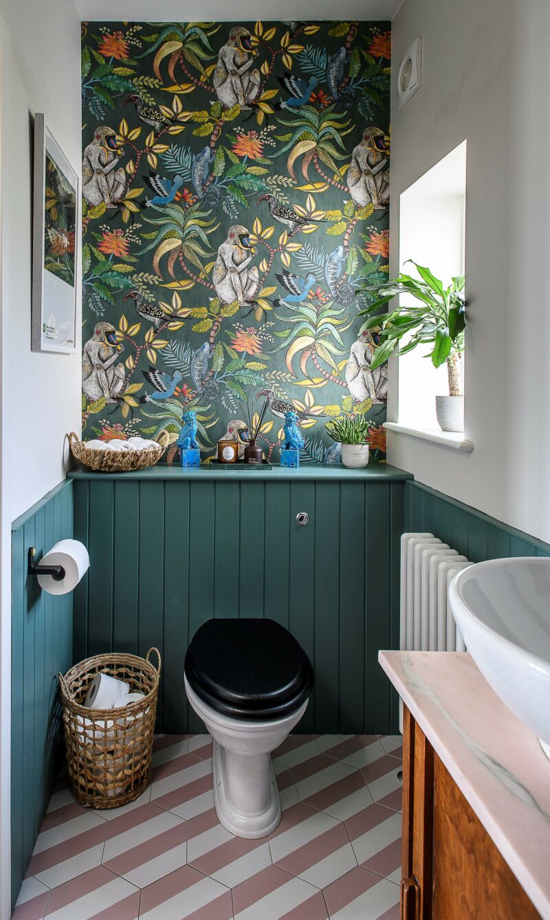 Downstairs toilet with jungle print wallpaper, green panelling, pink and white tiles.