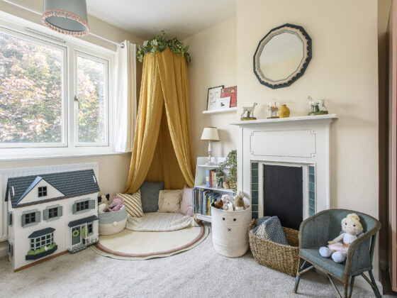 Children's bedroom with a feature fireplace, mustard yellow canopy and reading corner and toys.