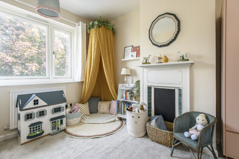 Children's bedroom with a feature fireplace, mustard yellow canopy and reading corner and toys.