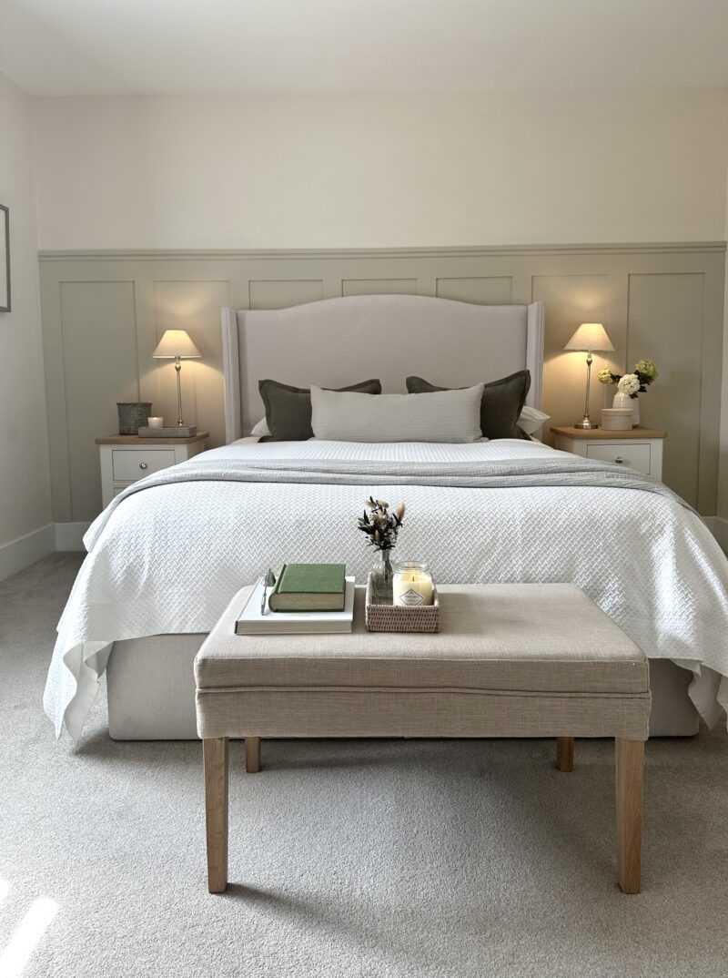 Cream winged upholstered bed in relaxing neutral bedroom with matching lamps on either side of the bed.