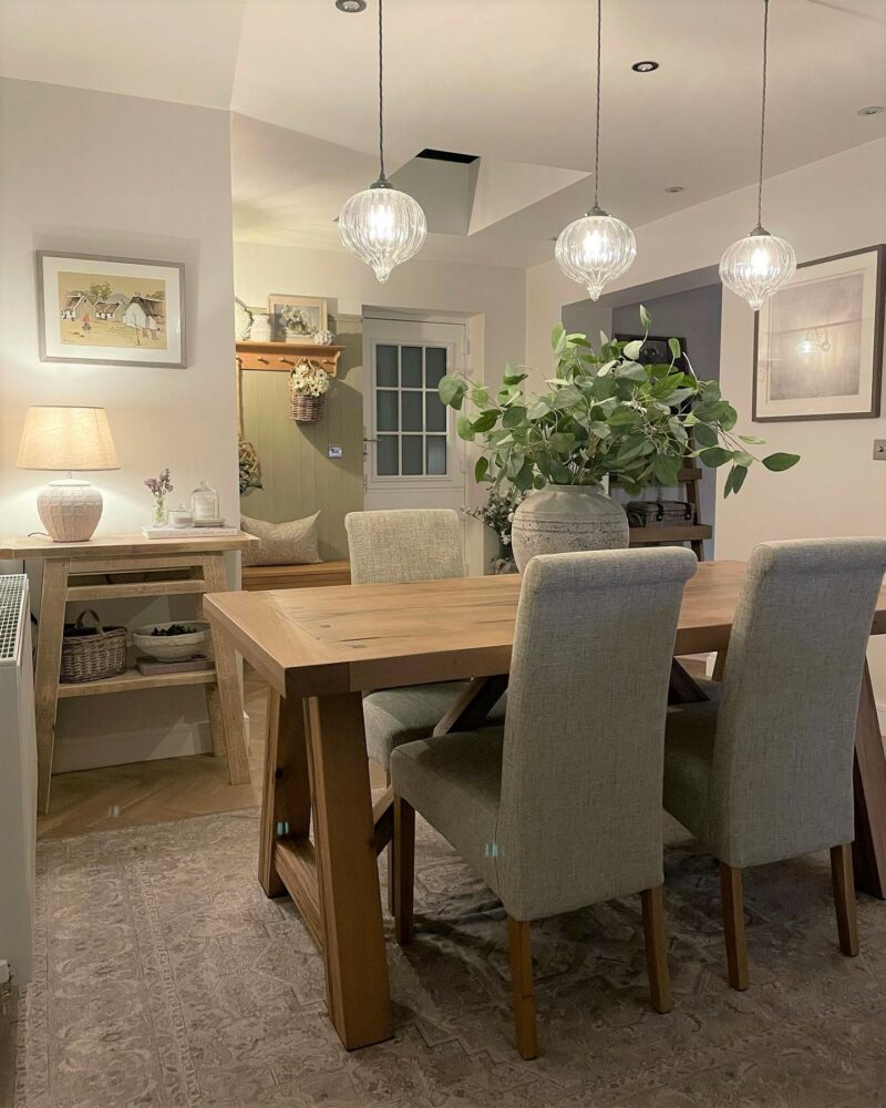 Oak dining table with scroll back upholstered dining chairs in a neutral dining space.