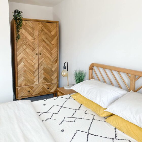 A bed, beside table and wardrobe-bedroom furniture-monochrome and yellow bedding-wooden bedside table-wooden triple wardrobe-wooden bed-bulb lamp