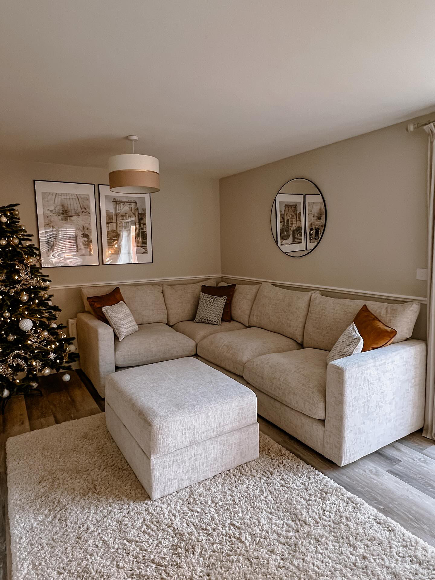 A sofa and Christmas tree-living room furniture-textured neutral rug-cream walls-cream corner sofa-storage footstool-Christmas tree with gold decorations-round wall mirror