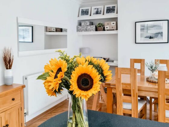 A dining table-dining room furniture-oak dining table and chairs-kitchen island-vase of sunflowers-white walls-long horizontal mirror-framed photography-oak sideboard-parquet flooring