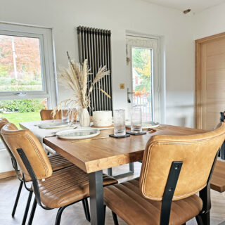 A dining table and chairs-dining room furniture-oak and metal dining table-leather dining chairs-place settings-tablescape-dried flowers-white walls-parquet floor