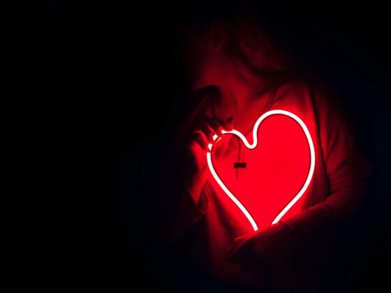 A neon red light up heart being held by a person in the dark