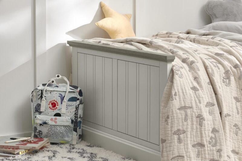 A bed-bedroom furniture-grey painted wooden bed-mushroom throw-patterned rucksack-yellow star cushion-neutral walls-stack of books-textured rug