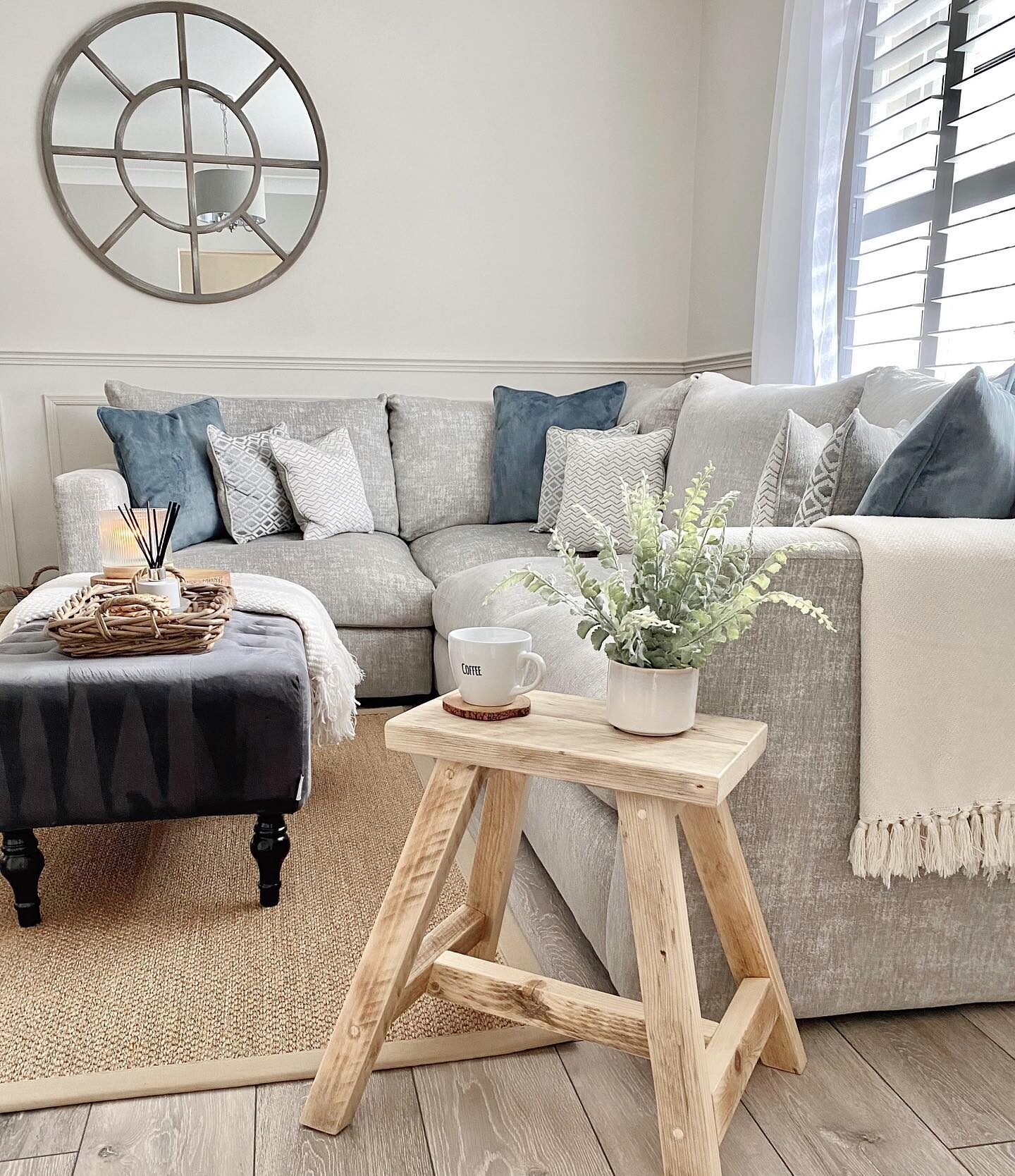 A modular corner sofa-living room furniture-pale grey corner sofa-denim blue accent cushions-dark grey footstool-rustic pale wooden stool-jute rug-cream walls-wooden floor-natural light