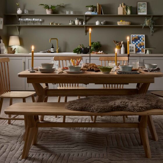 A dining table, display cabinet and bench-kitchen diner furniture-oak dining table set-neutral textured rug-spindle back chairs-olive green walls-sheepskin rug-tapered candles-soup bowls-bistro curtain-grey kitchen-open kitchen shelving-brass tap-autumnal tablescape