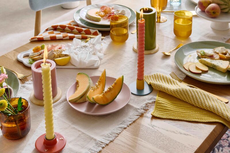 A dining table and chairs-dining room furniture-vintage patterned rug-pale oak dining table-upholstered dining chairs-colourful tablescape-fresh melon-checkerboard napkins-twisted candles-neutral table runner-fresh flowers-amber glassware-brass cutlery