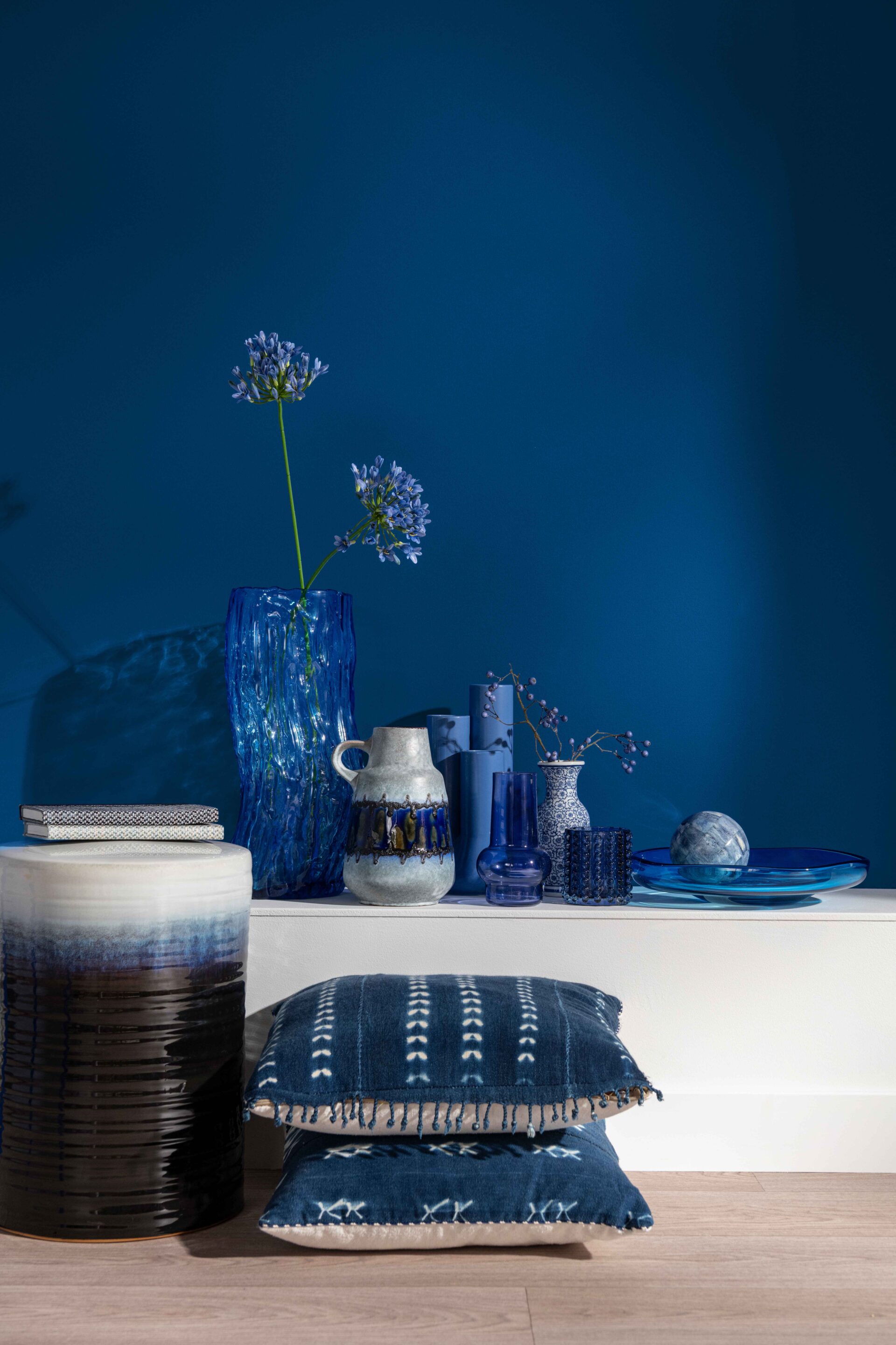 A shelf and vases-living room furniture-dark blue wall-wooden floor-white shelf-blue cushions-various blue vases