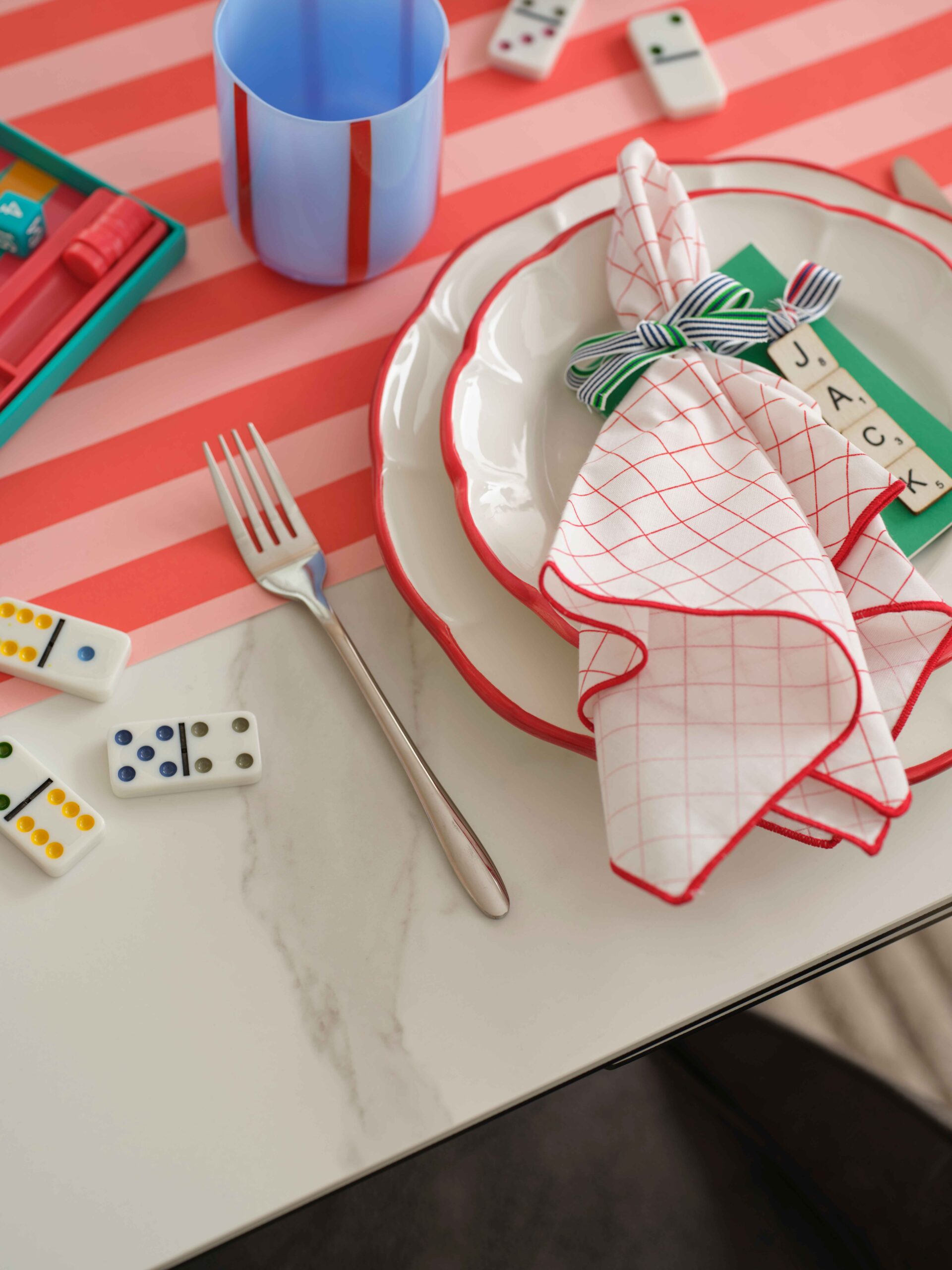 A dining table-dining room furniture-ceramic dining table-colourful tablescape-textured neutral rug-dominos-striped glass and table runner