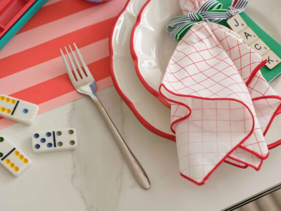 A dining table-dining room furniture-ceramic dining table-colourful tablescape-textured neutral rug-dominos-striped glass and table runner
