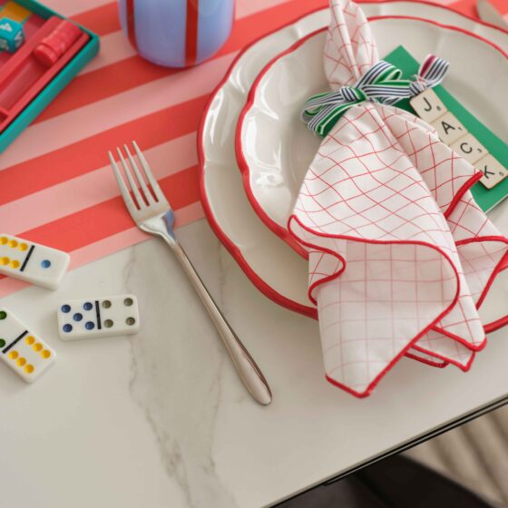 A dining table-dining room furniture-ceramic dining table-colourful tablescape-textured neutral rug-dominos-striped glass and table runner