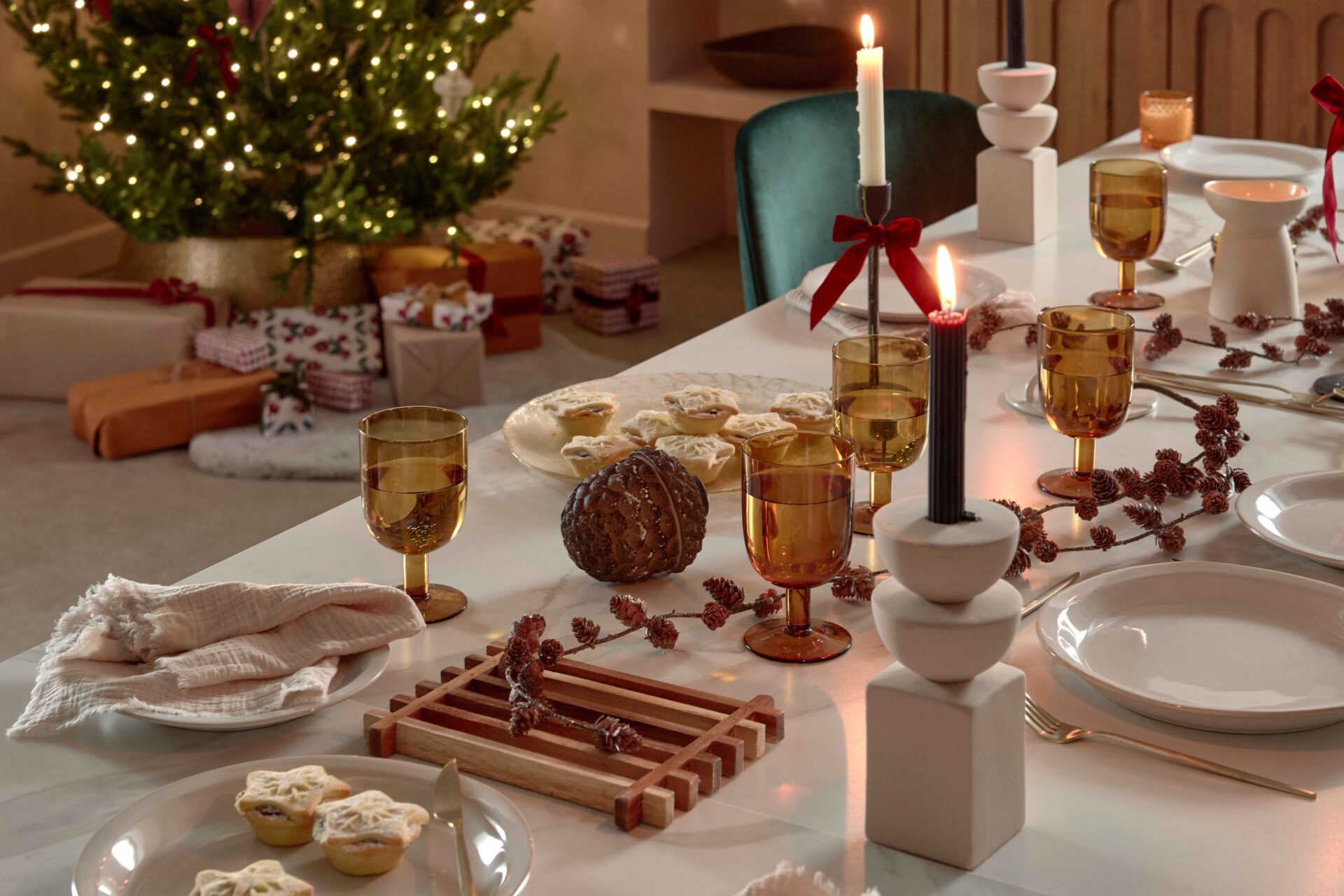 A dining table and chairs-dining room furniture-Christmas decorations-green velvet chairs-ceramic white dining table-Christmas tree- wrapped presents-mince pies-sculptural candle holders-festive tablescape