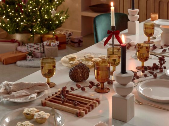 A dining table and chairs-dining room furniture-Christmas decorations-green velvet chairs-ceramic white dining table-Christmas tree- wrapped presents-mince pies-sculptural candle holders-festive tablescape