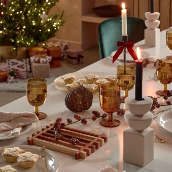 A dining table and chairs-dining room furniture-Christmas decorations-green velvet chairs-ceramic white dining table-Christmas tree- wrapped presents-mince pies-sculptural candle holders-festive tablescape