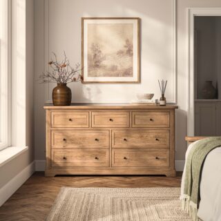 A chest of drawers-bedroom furniture-natural oak chest of drawers-parquet flooring-jute rug-brown vase-neutral panelled walls-subtle wall art-green throw-neutral bedding