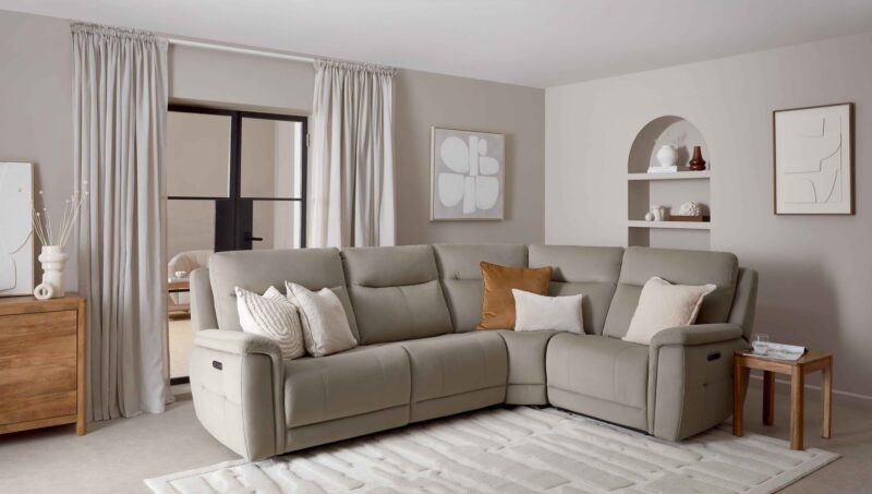 A corner sofa-living room furniture-neutral corner recliner sofa-tan cushion-cream cushions-arched built in shelving-abstract neutral wall art-textured cream rug-concrete flooring-wooden side table-wooden sideboard-crittal doors-draped neutral curtains