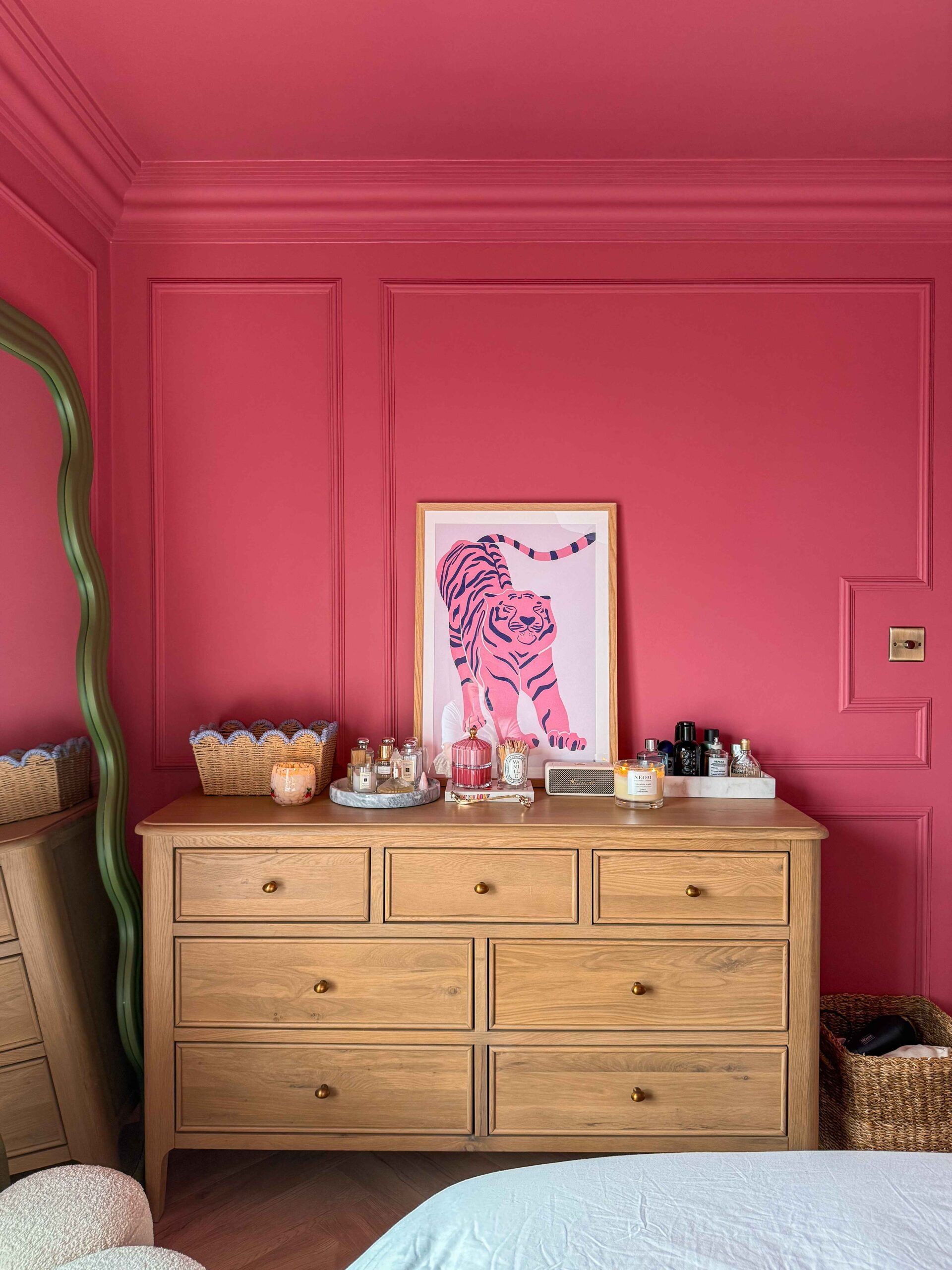 A chest of drawers-bedroom furniture-bright pink walls with panelling-oak chest of drawers-green wiggle floor standing mirror-parquet flooring-tiger wall art-scallop edge storage basket-marble trays-perfume-candles-skincare