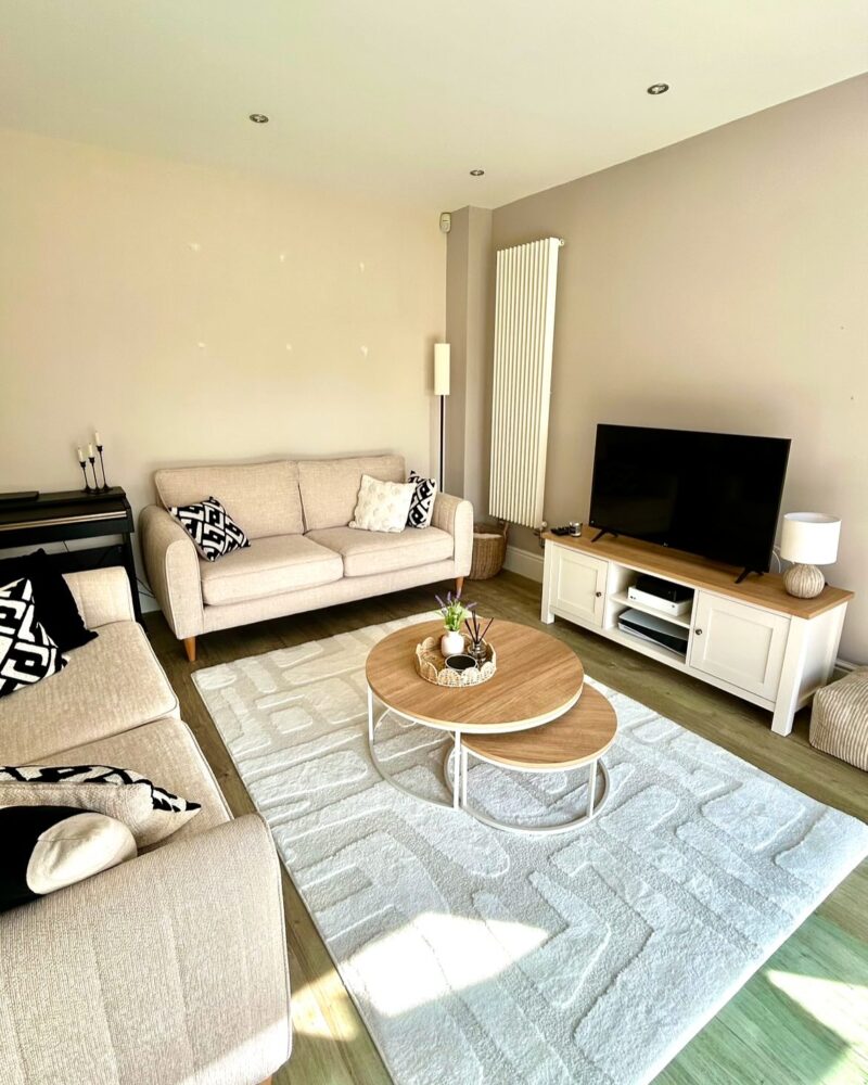 Sofas, coffee table and TV unit-living room furniture-coffee round nest of tables-neutral geometric rug-cream 2 seater sofas-monochrome cushions-cream and wooden TV unit-neutral table lamp-black piano keyboard-vertical white radiator