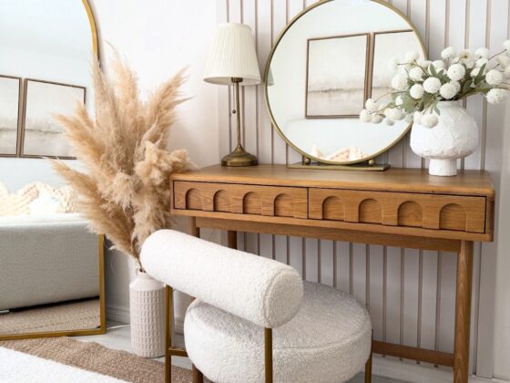 A dressing table-bedroom furniture-wooden console table with arch detail-boucle dressing table chair-round brass mirror-table lamp-vase of white flowers-vase of pampas grass-fluted wall panelling-white walls-floor standing arched mirror-jute rug