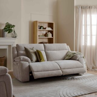 A sofa, bookcase, and armchair-neutral reclining sofa-sheer draped curtains-wooden bookcase-neutral textured rug-parquet wooden floor-neutral reclining armchair-off white fireplace-off white walls-woven storage basket