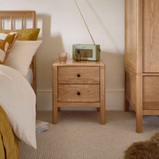 A bedside table, wardrobe, and bed-bedroom furniture-natural oak bedside table-natural oak wardrobe-wooden bed with spindle headboard-brown faux sheepskin rug-neutral carpet-cream walls-gold bedding-white bed linen-green retro radio-glass cup of tea