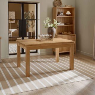 A wooden dining table and small dresser-dining room furniture-natural oak wooden dining table-neutral walls-natural oak small wooden dresser-draped neutral curtains-crittall internal door-striped jute rug-wooden floor-stone painted sideboard-champagne glasses-abstract neutral artwork-brown ceramic vase-tray