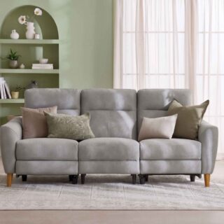 A sofa and console table-living room furniture-grey leather recliner sofa-earthy scatter cushions-vintage style rug-sheer curtains-sage green walls-built in arched shelving-oak console table-potted houseplant-cream vase with white flowers-woven basket-stacked books