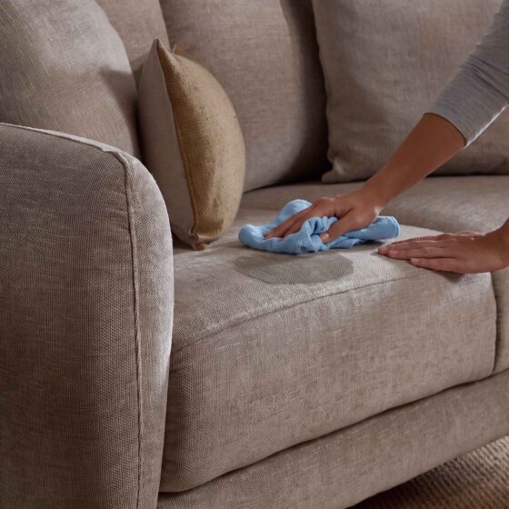 A sofa and side table-living room furniture-beige sofa-scatter cushions-blue cloth-grey top-person cleaning-wooden side table-sisial carpet