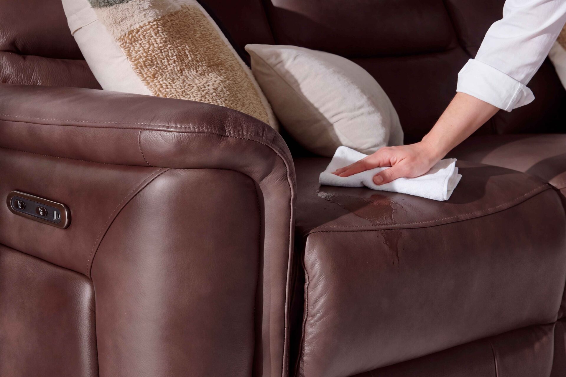 A leather sofa-living room furniture-burgundy leather recliner sofa-cream cushion-textured block print cushion-person's arm-white shirt-white cloth