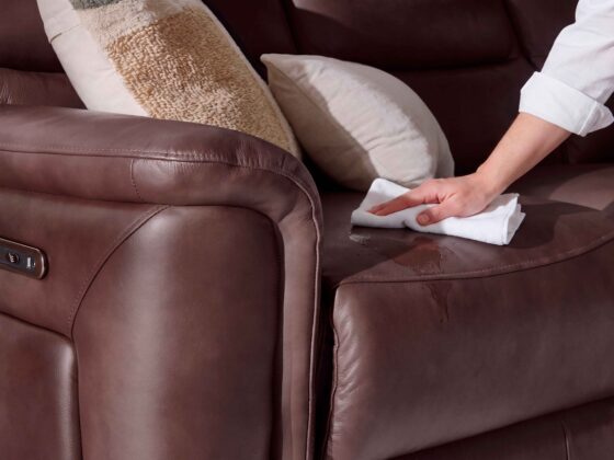 A leather sofa-living room furniture-burgundy leather recliner sofa-cream cushion-textured block print cushion-person's arm-white shirt-white cloth