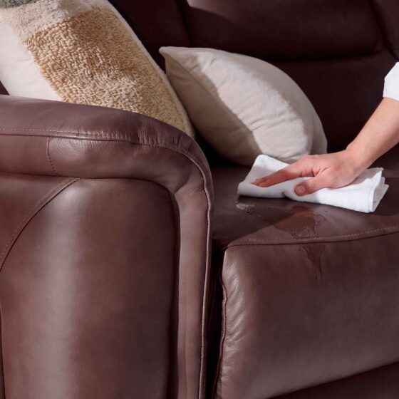 A leather sofa-living room furniture-burgundy leather recliner sofa-cream cushion-textured block print cushion-person's arm-white shirt-white cloth