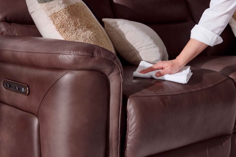 A leather sofa-living room furniture-burgundy leather recliner sofa-cream cushion-textured block print cushion-person's arm-white shirt-white cloth