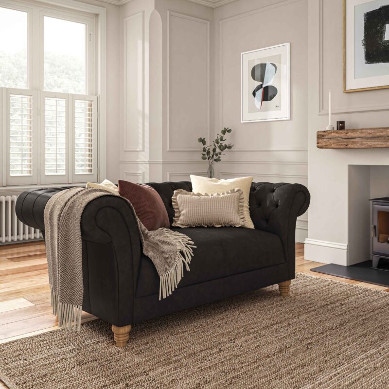 A sofa-living room furniture-black leather chesterfield style sofa-neutral cushions-neutral walls with panelling and beading-abstract artwork-jute rug-fireplace-window shutters-radiator-neutral throw