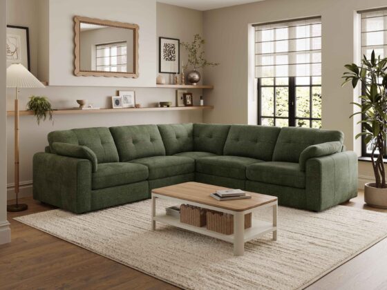 A corner sofa, coffee table, and nest of tables-living room furniture-dark green corner modular sofa-wooden and cream painted coffee table with shelf-wooden and cream painted nest of tables-cream textured rug-dark wooden floor-scallop edged mirror-built in wooden sheving-floor standing lamp-framed wall art-potted house plant-crittall windows-sheer blind