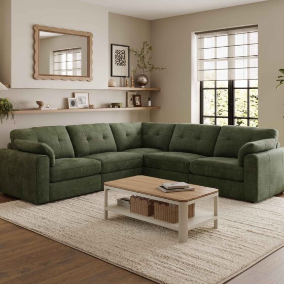 A corner sofa, coffee table, and nest of tables-living room furniture-dark green corner modular sofa-wooden and cream painted coffee table with shelf-wooden and cream painted nest of tables-cream textured rug-dark wooden floor-scallop edged mirror-built in wooden sheving-floor standing lamp-framed wall art-potted house plant-crittall windows-sheer blind