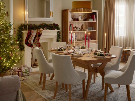 A dining table, chairs, bench, and dresser-dining room furniture-a wooden dining table-beige fabric dining chairs-large wooden dresser-wooden bench-draped curtains-marble patterned crackers-gold cutlery-christmas styling-white gravy boat-tapered candles in red and cream-delicate blue scalloped glassware-white crockery-off white fireplace-festive garland-christmas tree-handmade stockings-mustard tassel ceiling lampshade-wooden bench-vintage style rug-wooden parquet flooring